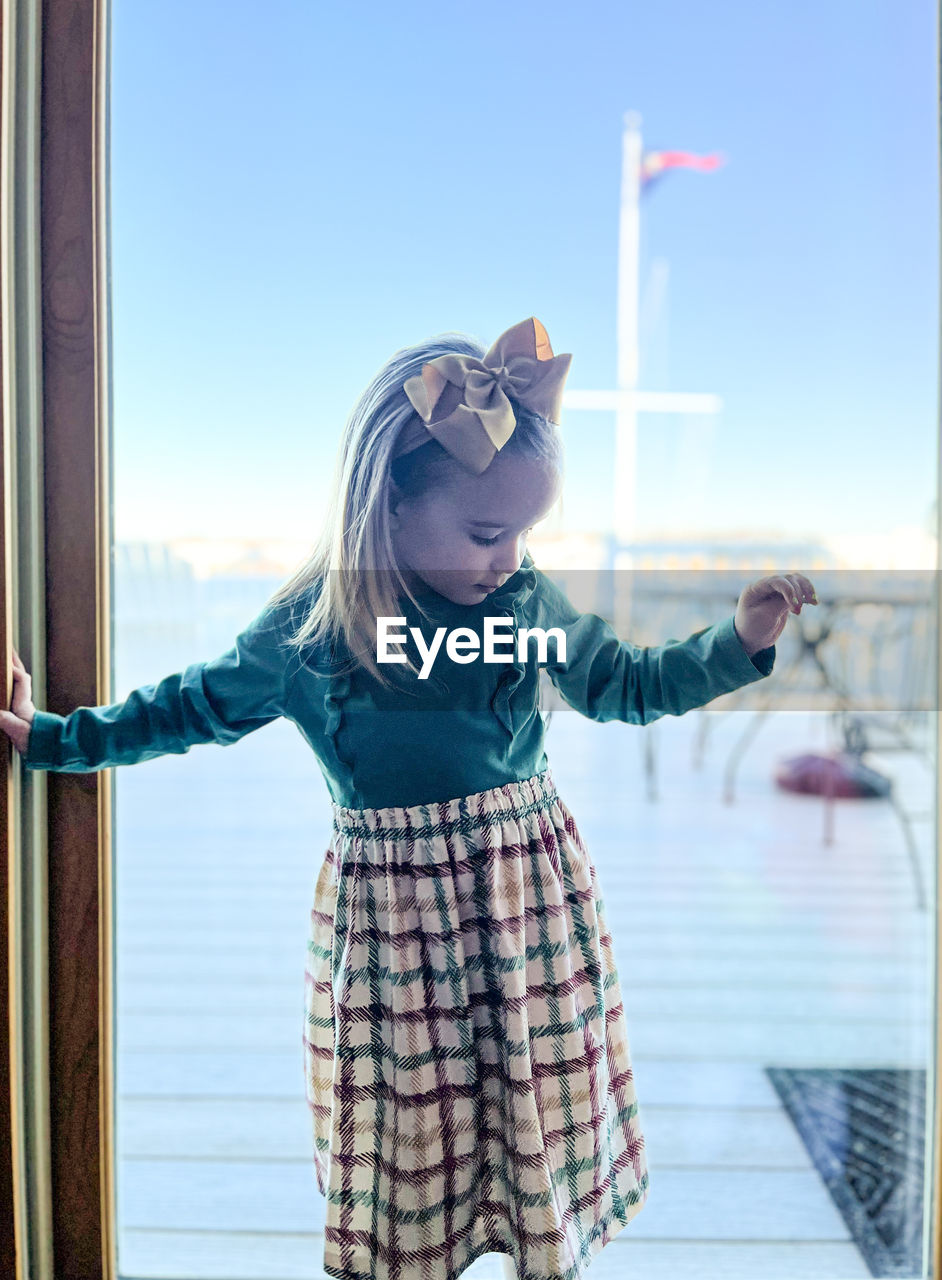 3-year-old girl in dress balancing at yacht club window