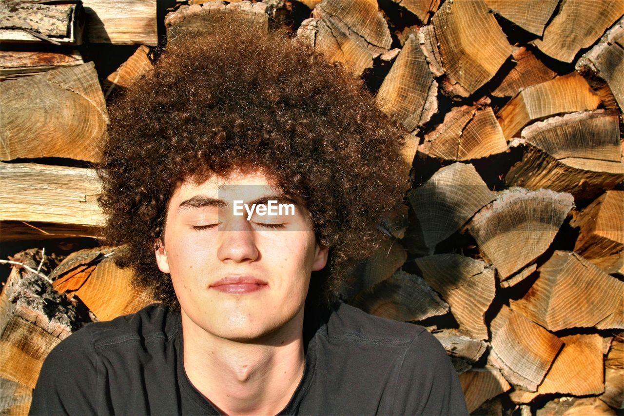 Close-up of young man with curly hair against stacked logs