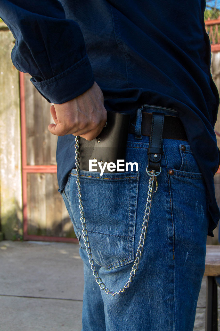 MIDSECTION OF MAN HOLDING CAMERA WHILE STANDING AGAINST BLUE WALL