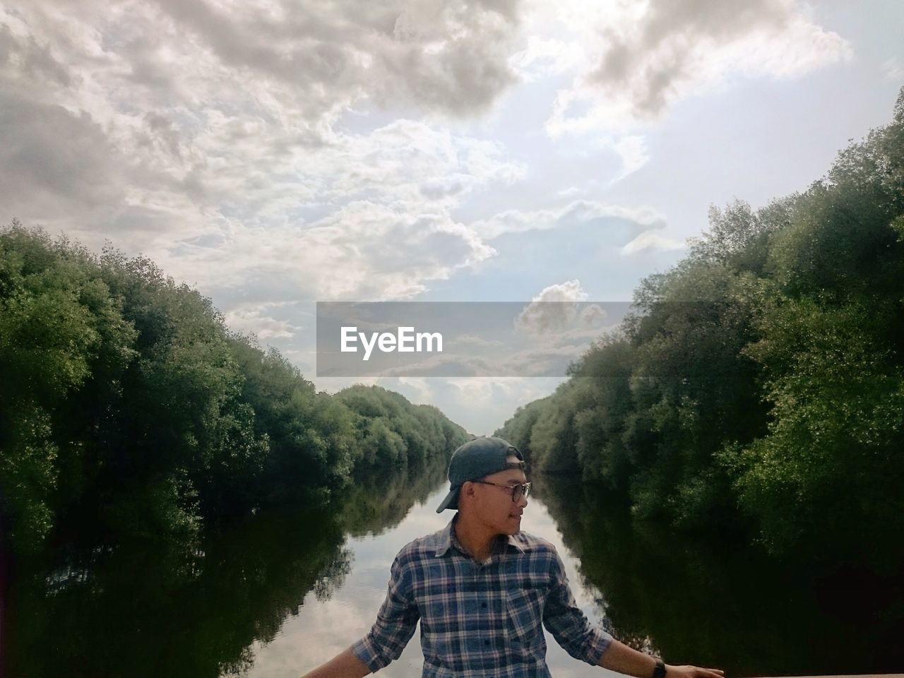 Young man standing against calm lake with reflection of trees