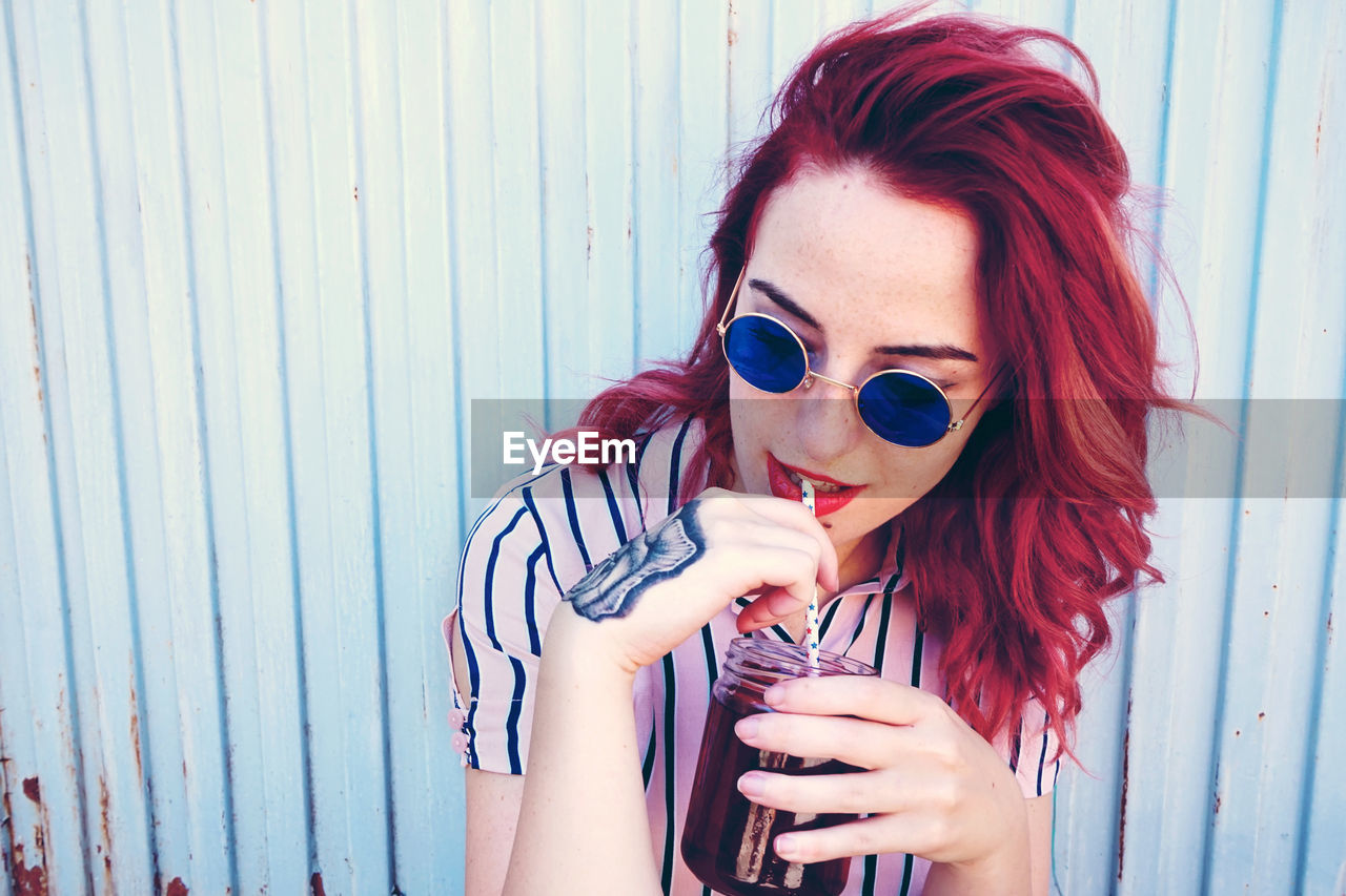 Woman having drink while sitting by wall