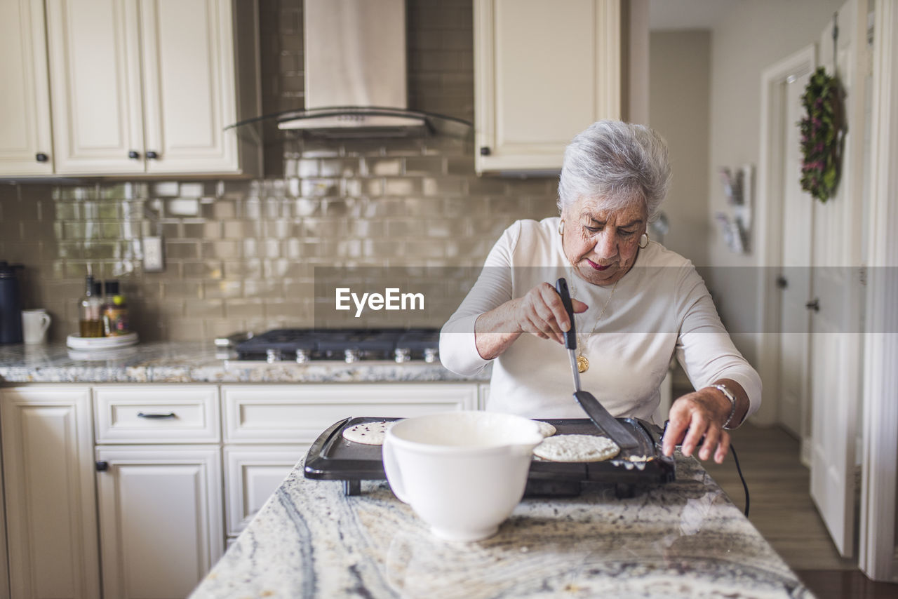 Portrait of senior woman cooking pancakes for breakfast