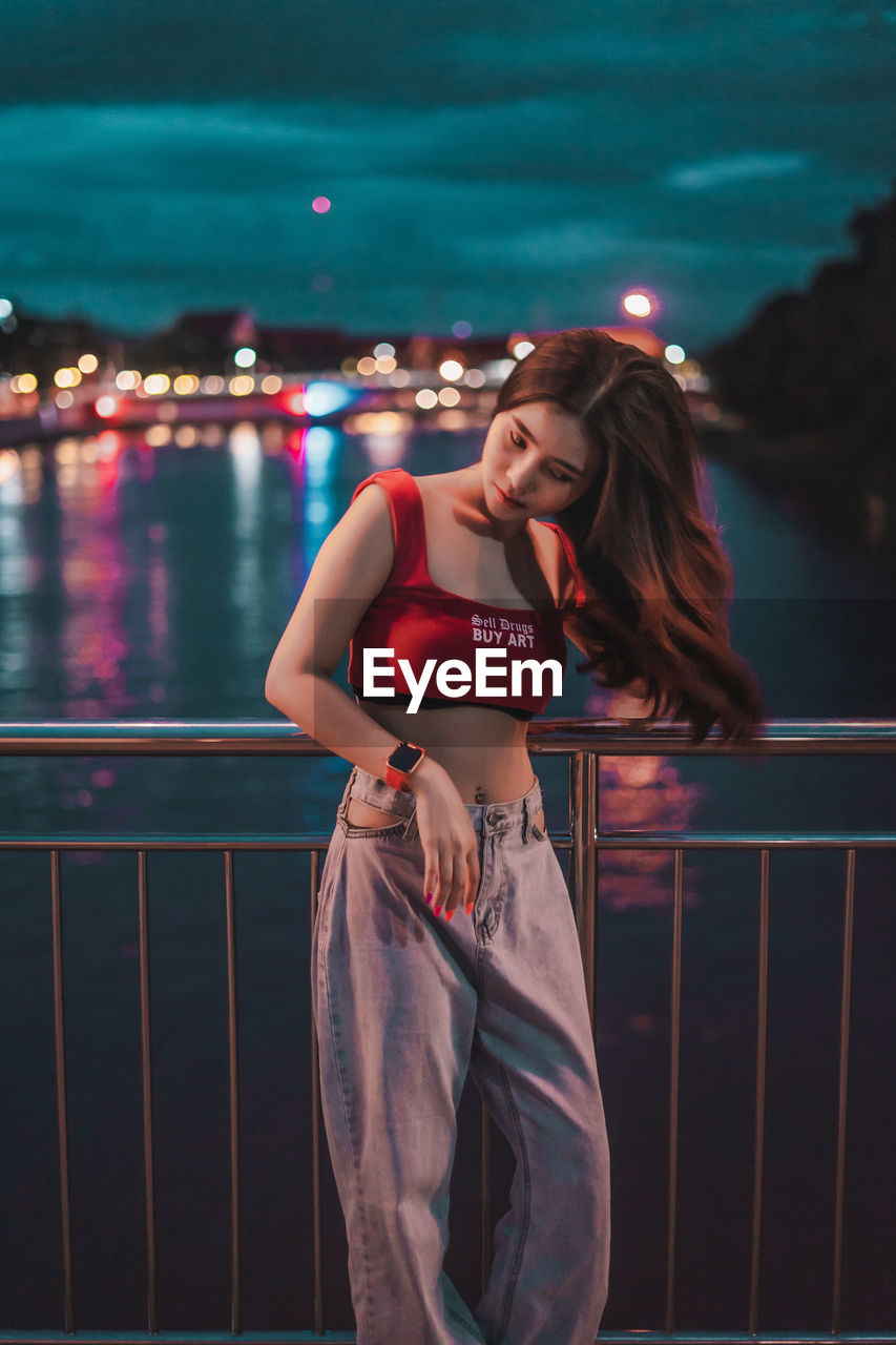 Smiling young woman standing on bridge over river at night