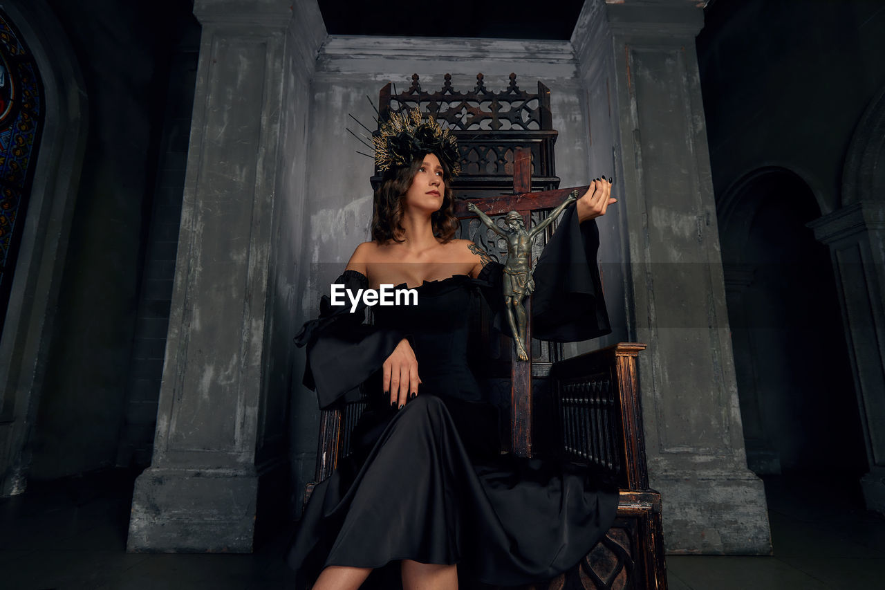 Low angle view of beautiful woman sitting on chair with cross