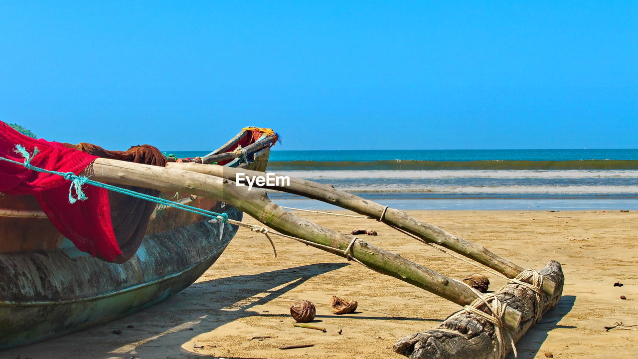 Driftwood on beach against clear blue sky