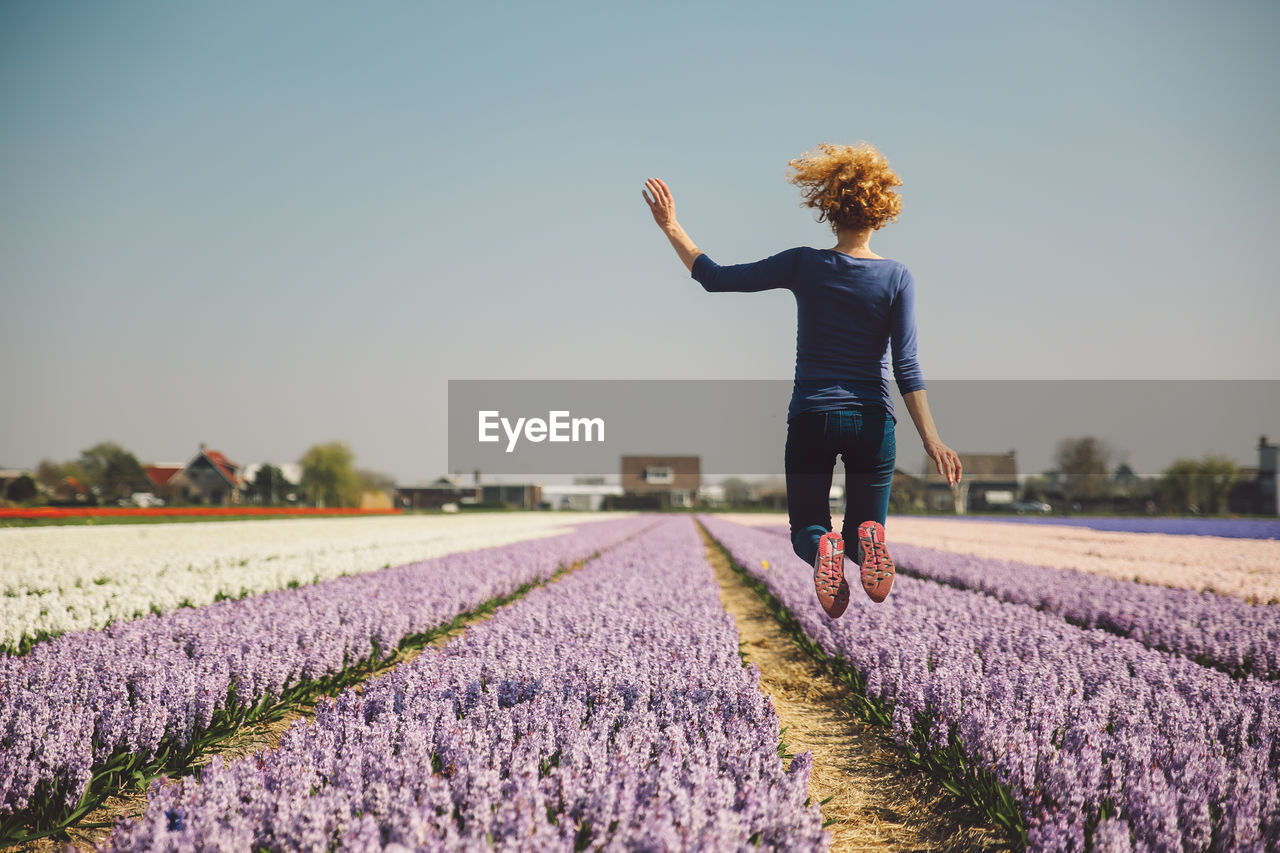 Woman jumping on field against clear sky