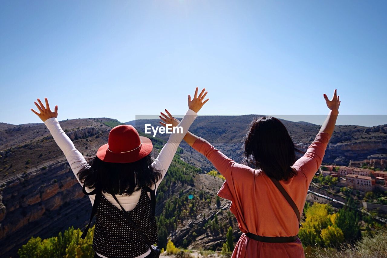 Rear view of friends with arms raised against clear sky