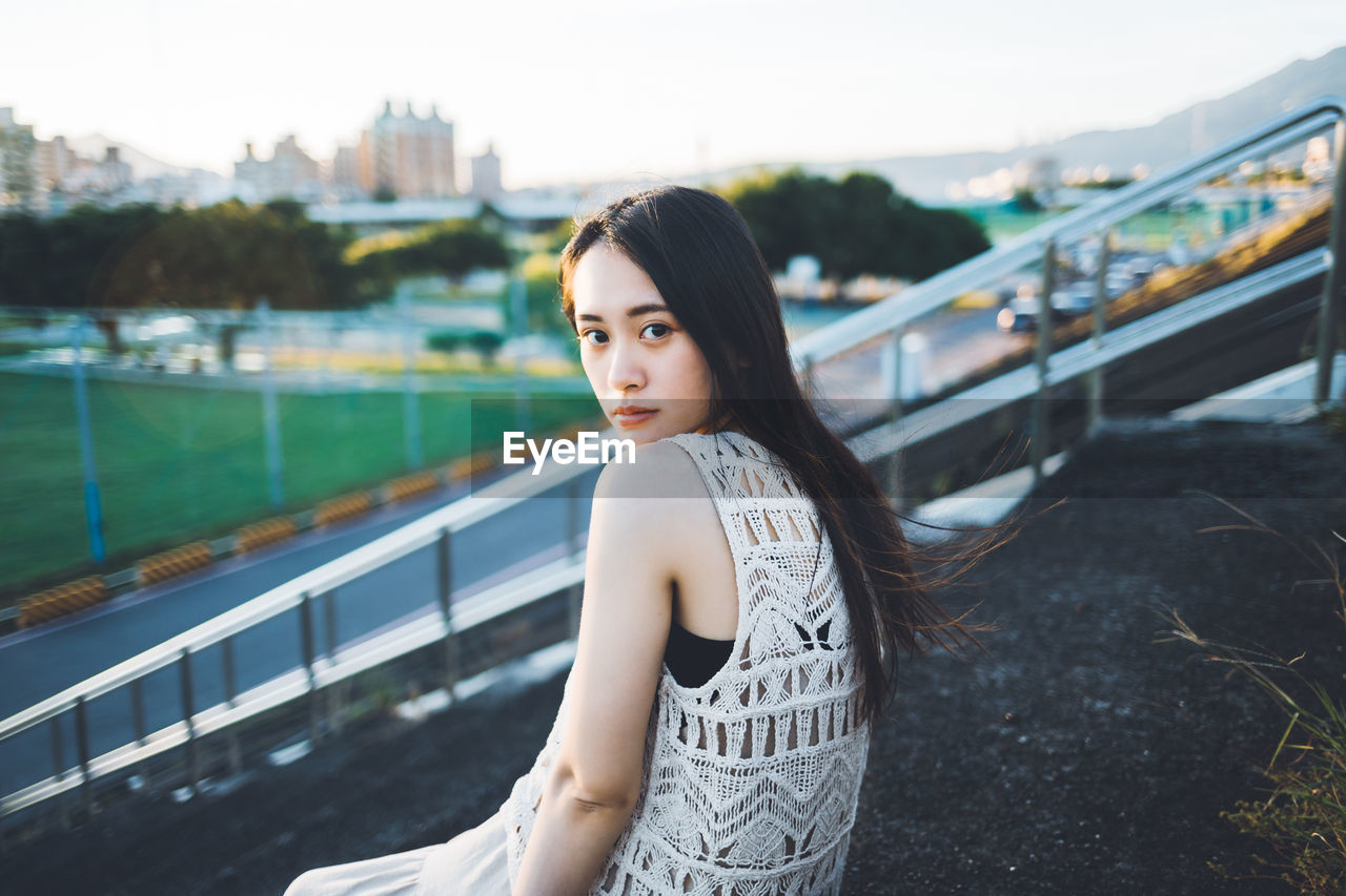 PORTRAIT OF YOUNG WOMAN AGAINST RAILING AGAINST WATER