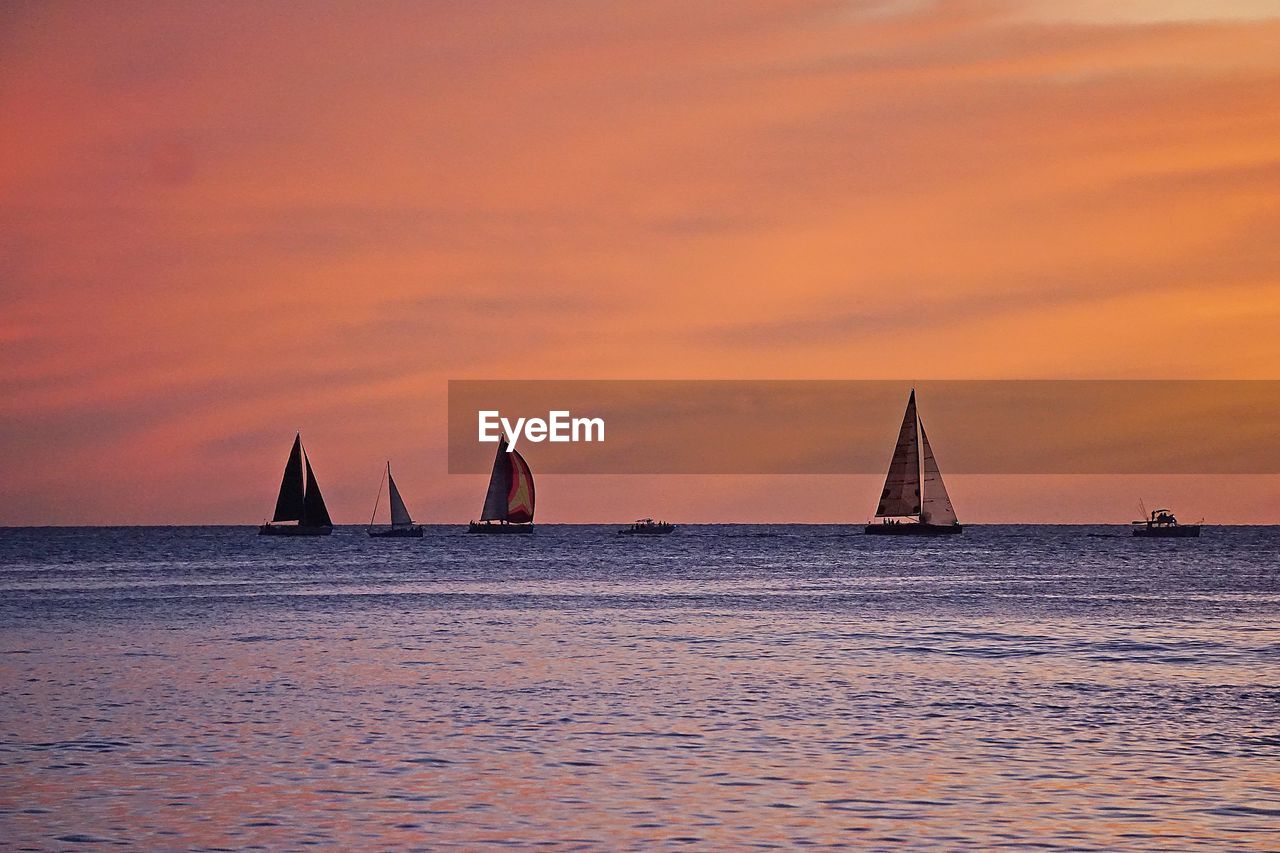 Sailboats sailing on sea against orange sky