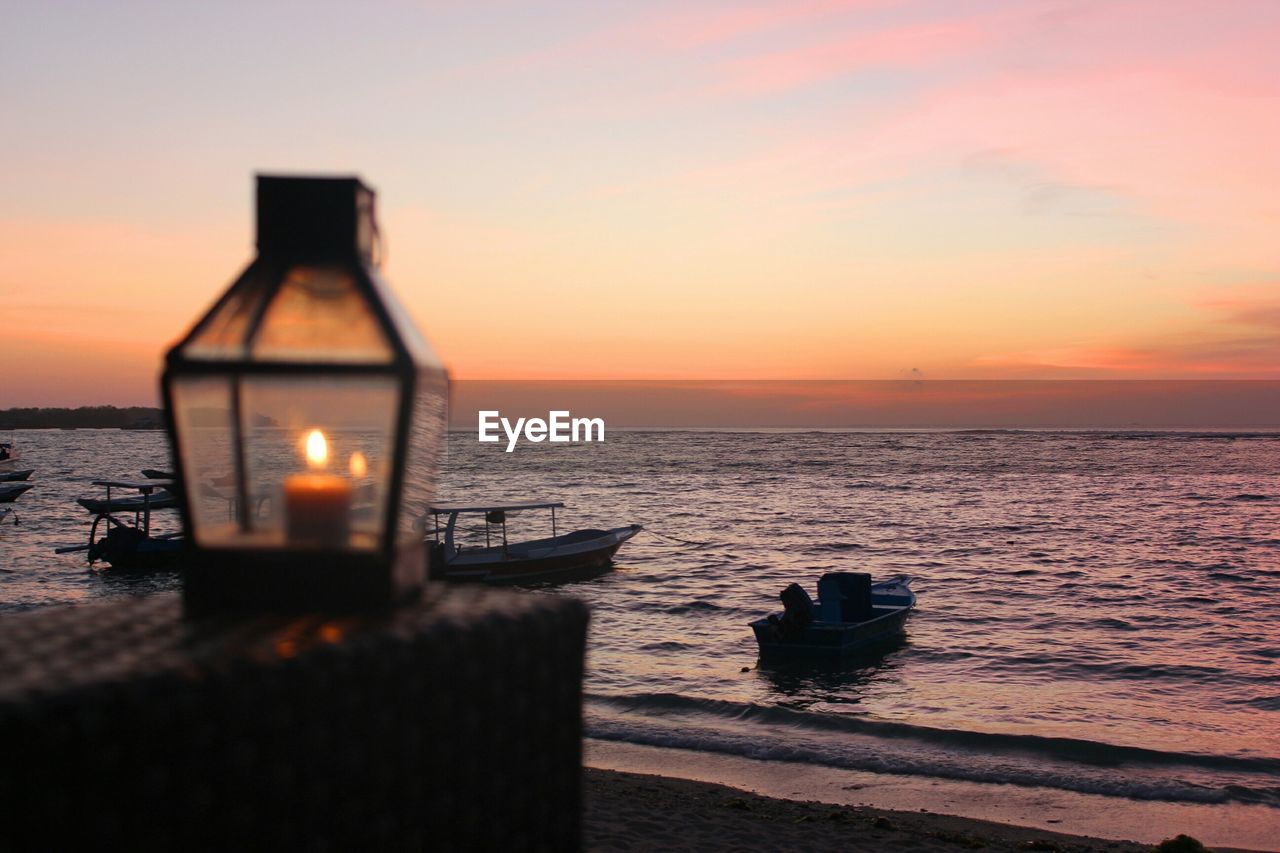 Tea light candle against boats moored at sea during sunset