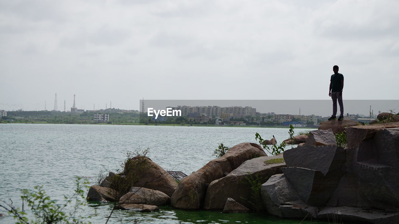 REAR VIEW OF MAN STANDING ON ROCK