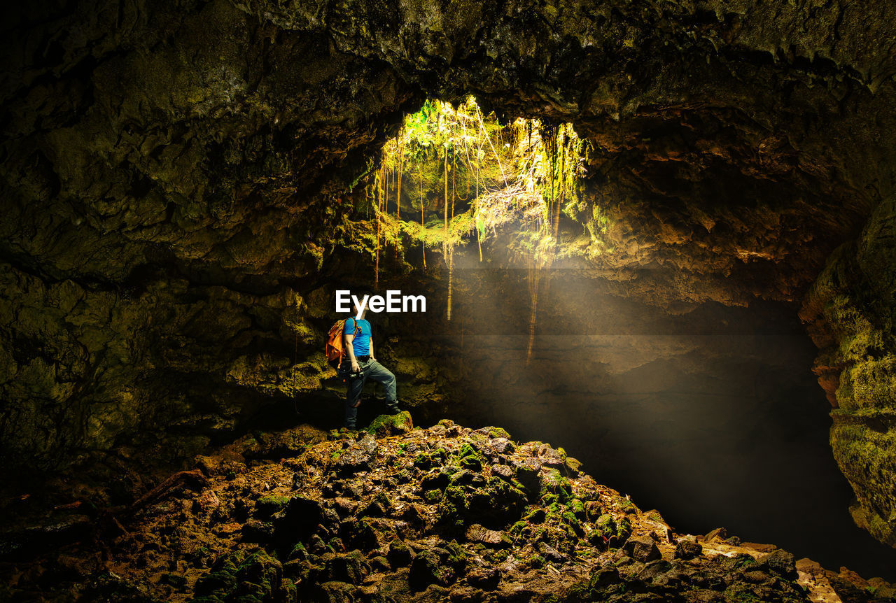 Man standing below sunlight streaming in cave