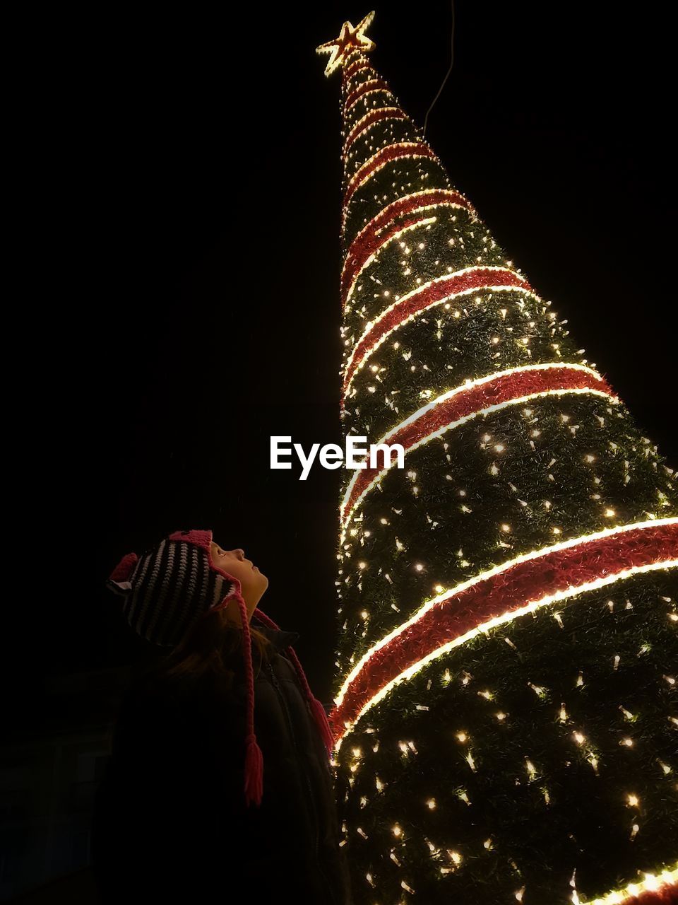 Low angle view of boy looking at illuminated christmas tree against sky during night