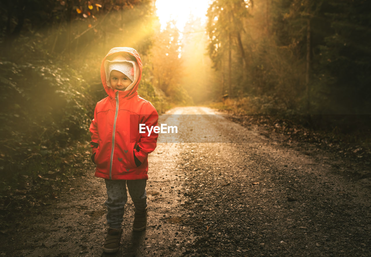 Child standing on wet path in moody forest. sun beams in background.
