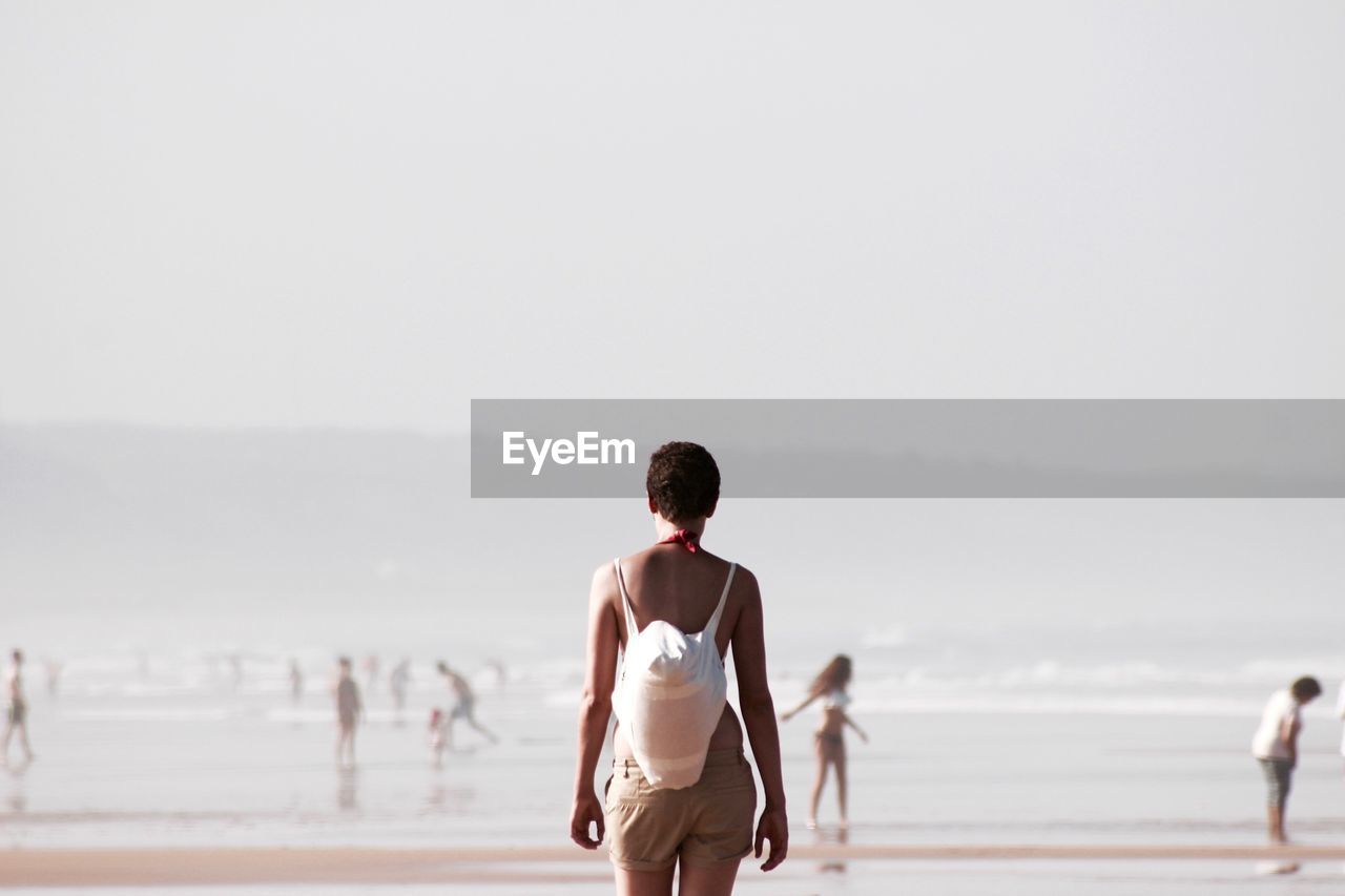 Rear view of woman carrying bag while walking on beach during foggy weather