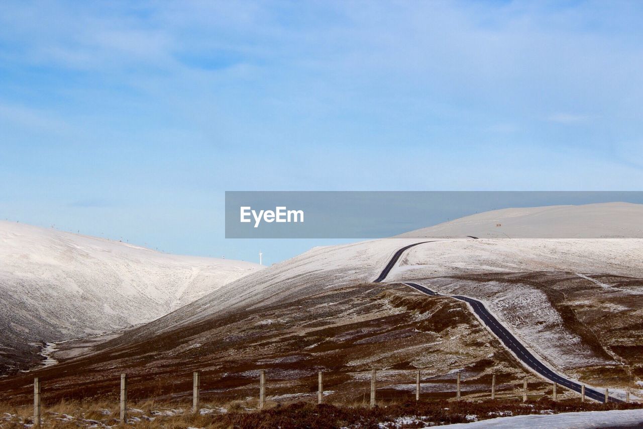 Scenic view of road across snowy mountains lagainst sky