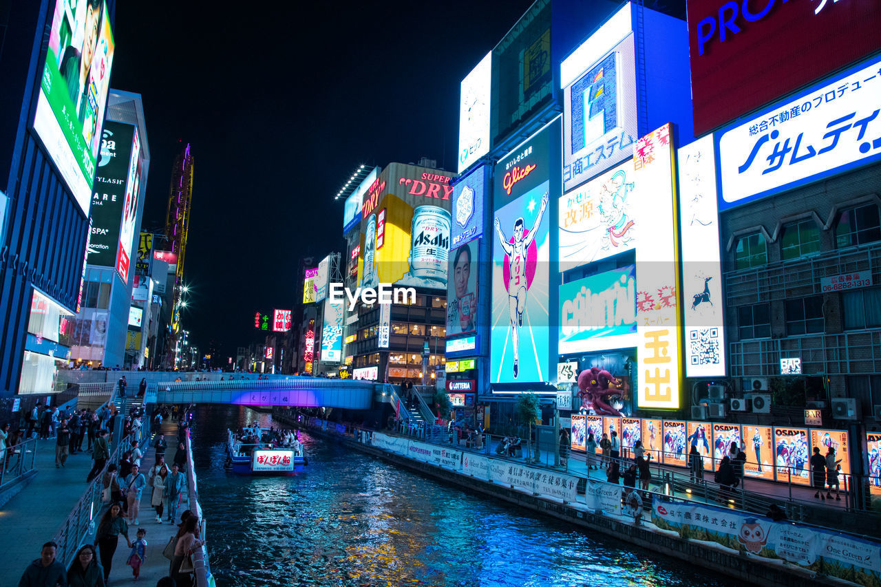 PEOPLE IN ILLUMINATED BUILDING BY CANAL AT NIGHT