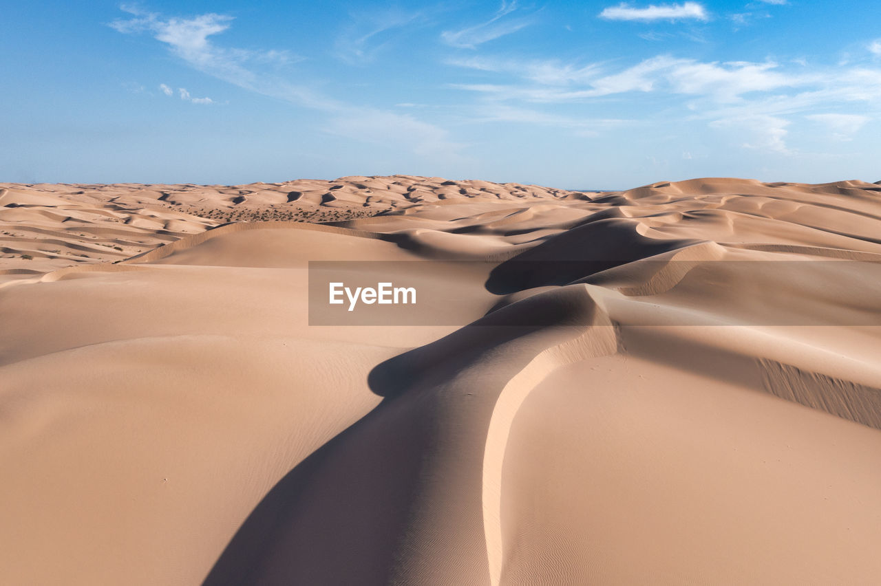 Large sand dunes with texture, patterns, light and shadow. blue sky with white clouds.