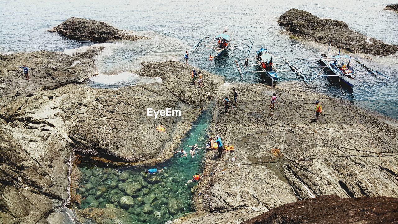 HIGH ANGLE VIEW OF PEOPLE WORKING ON ROCK AT BEACH