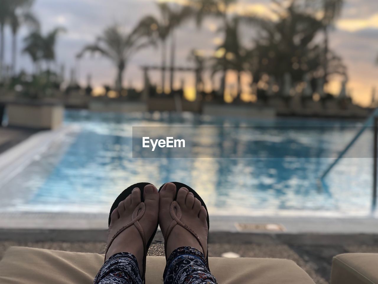 Low section of woman relaxing at poolside during sunset