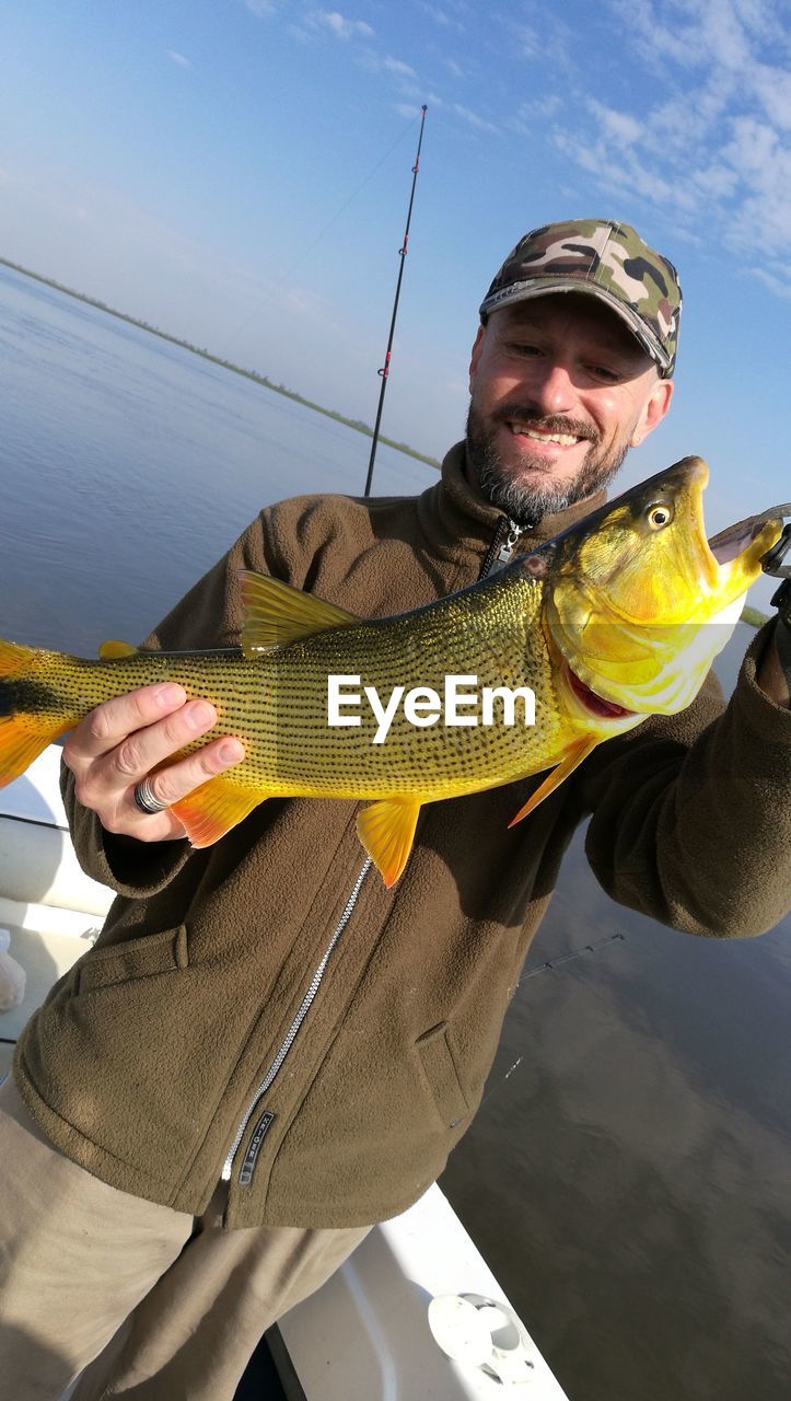 Man holding big yellow fish while standing in boat against sea