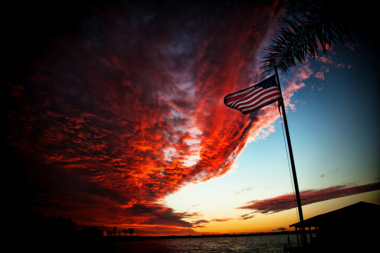 Low angle view of american flag against dramatic sky during sunset