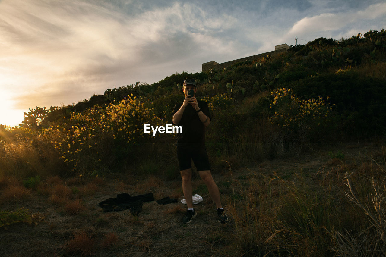 Full length of man with camera standing on field against sky