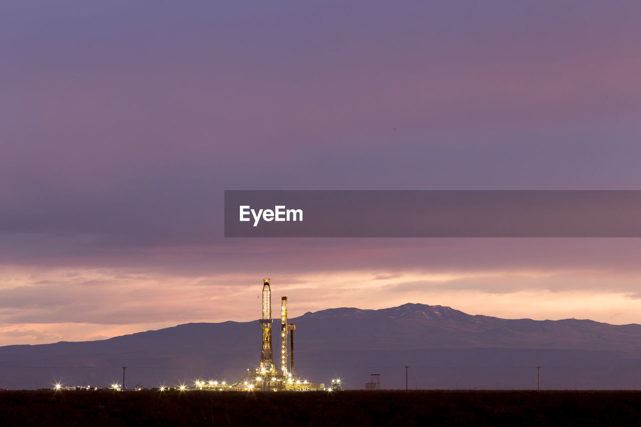 Drilling rig on field against cloudy sky
