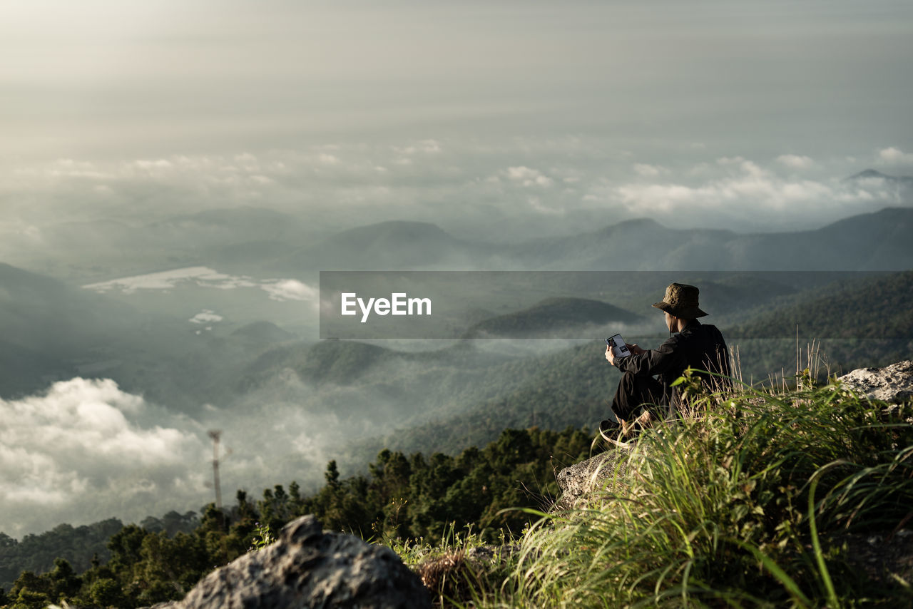 Man sitting on mountain against sky