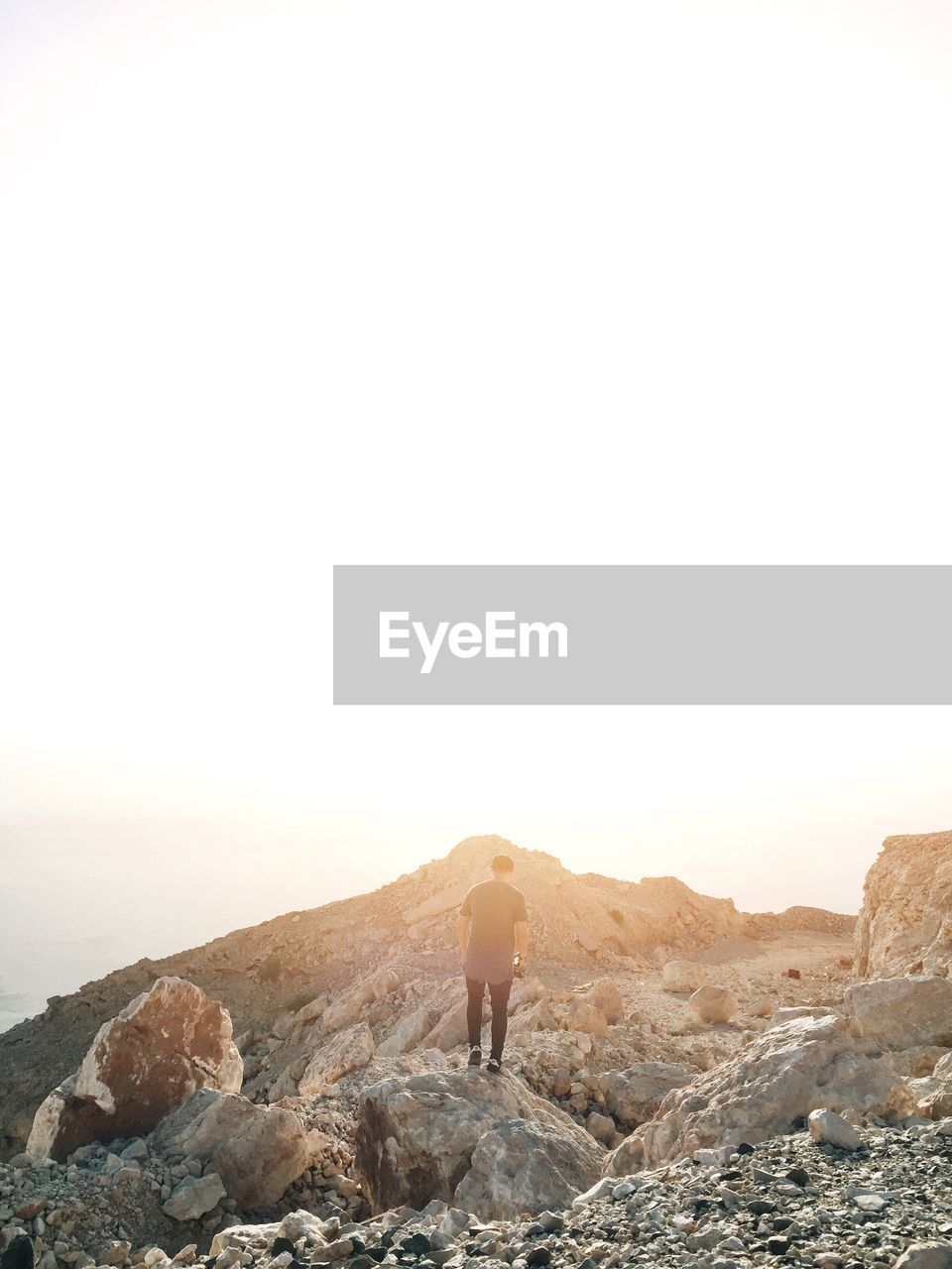 Rear view of man standing on rock against sky