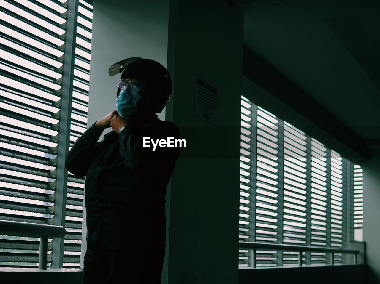 Low angle view of man wearing flu mask standing against window