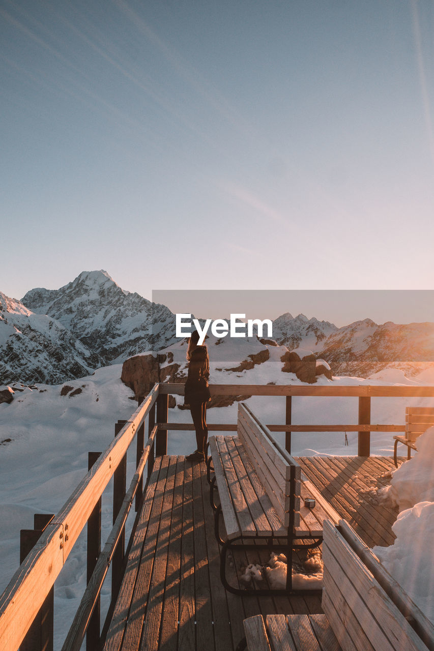 Rear view of person standing on snowcapped mountain against sky