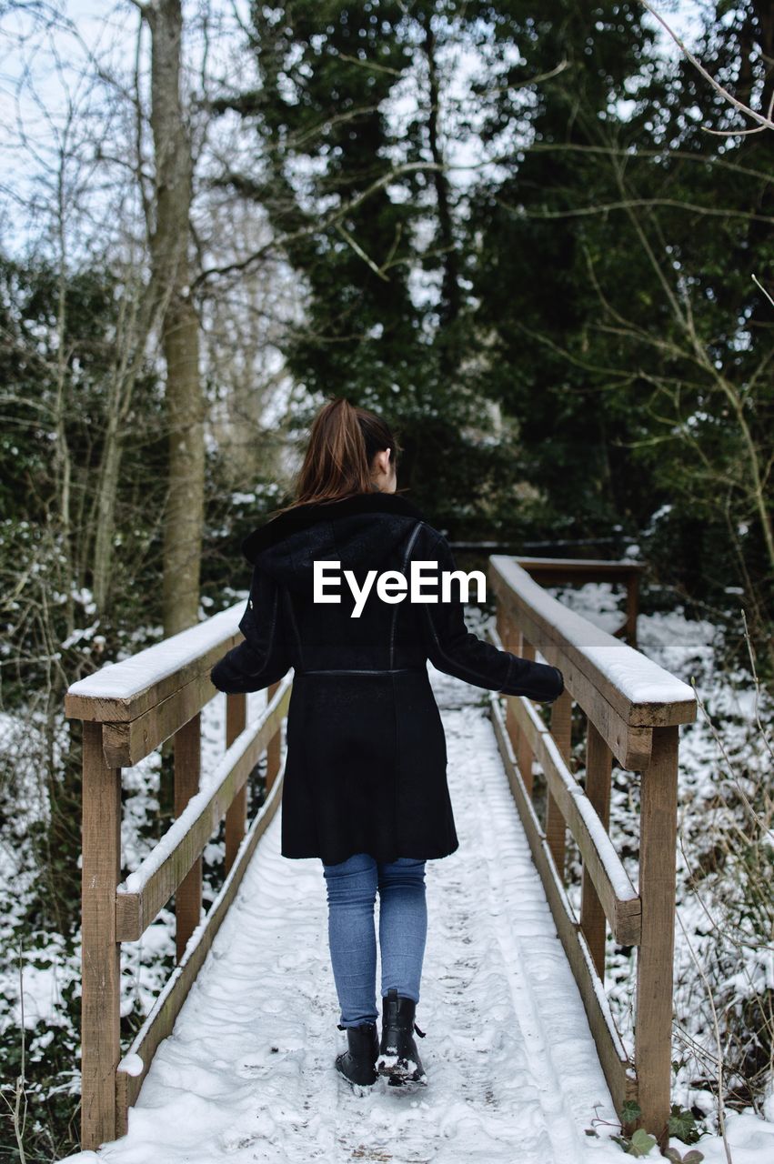 Rear view of young woman standing snow covered footbridge