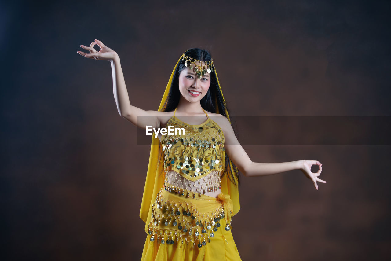 PORTRAIT OF A SMILING YOUNG WOMAN STANDING AGAINST YELLOW