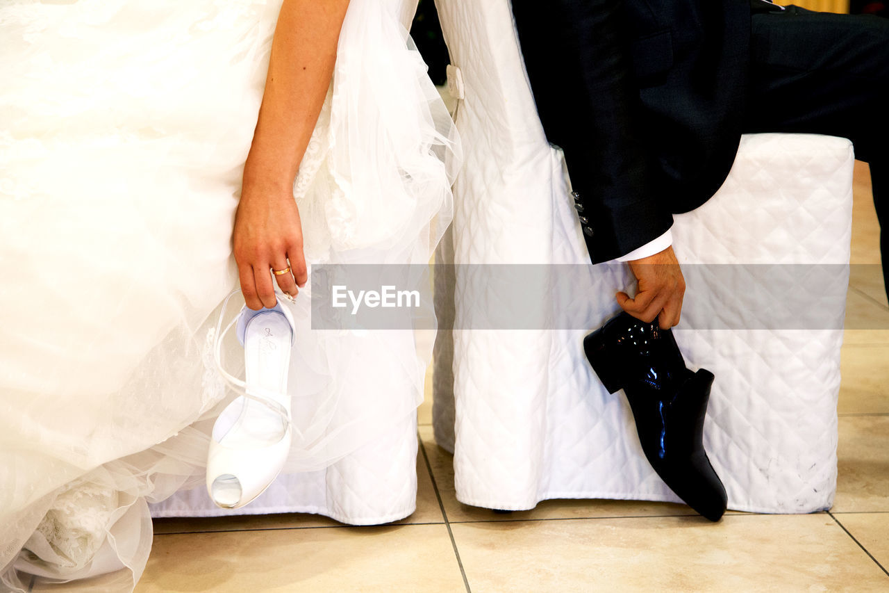 LOW SECTION OF MAN AND WOMAN HOLDING WHITE DRESS