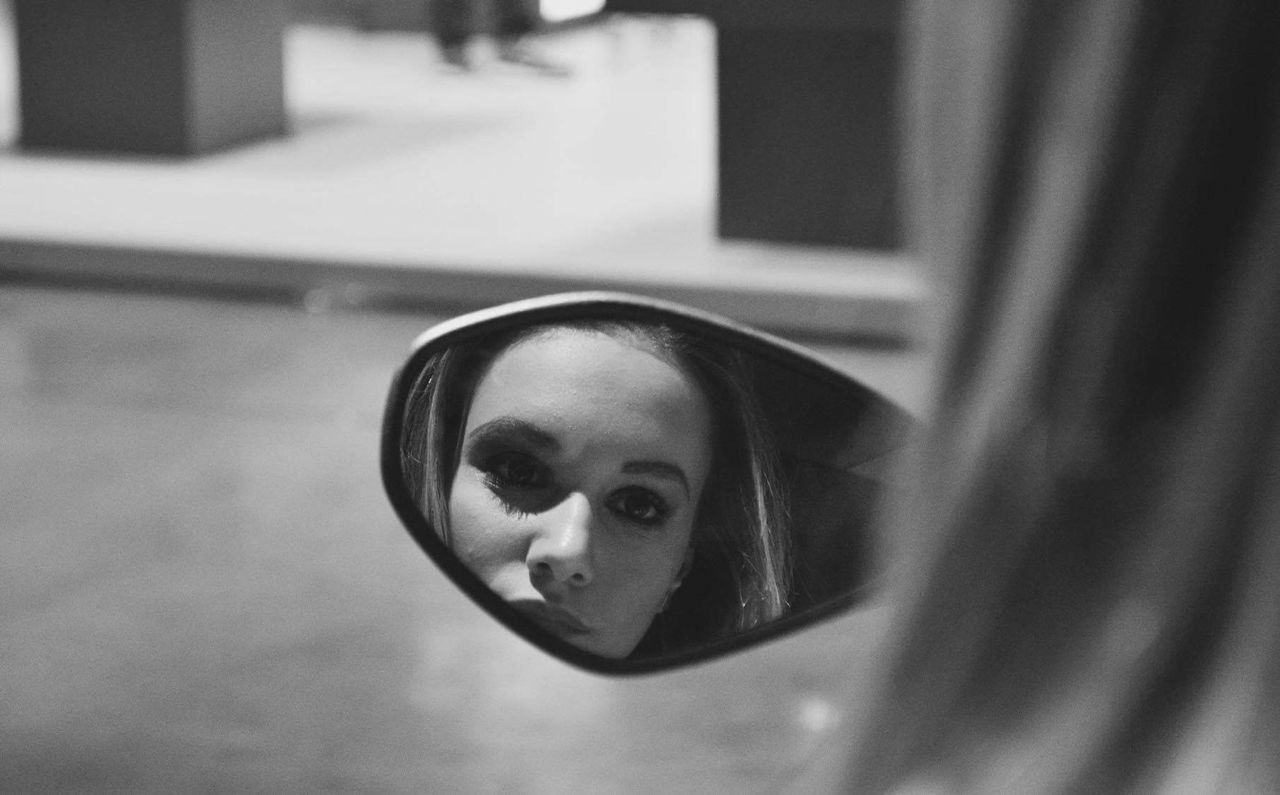 Young woman reflecting in side-view mirror of car
