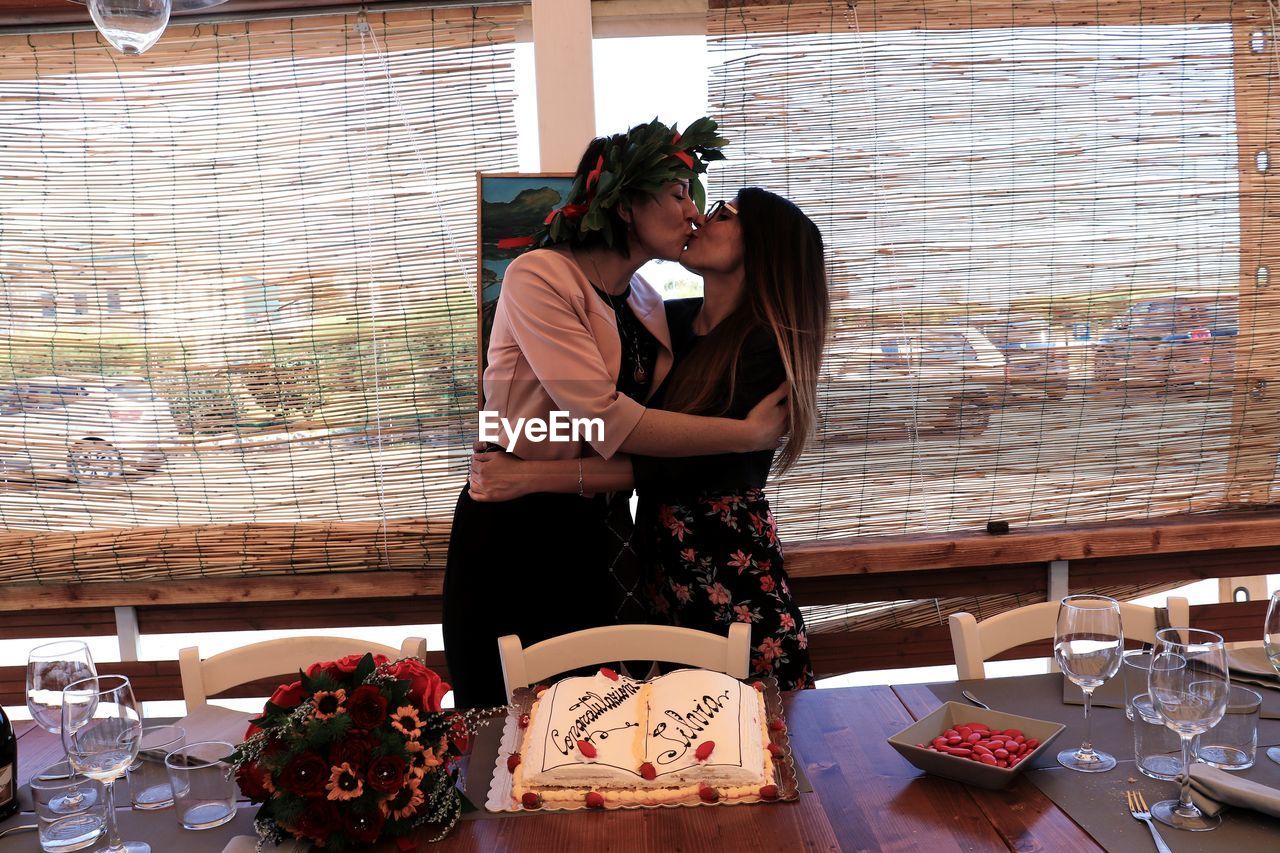 Lesbian couple kissing while standing by window during celebration