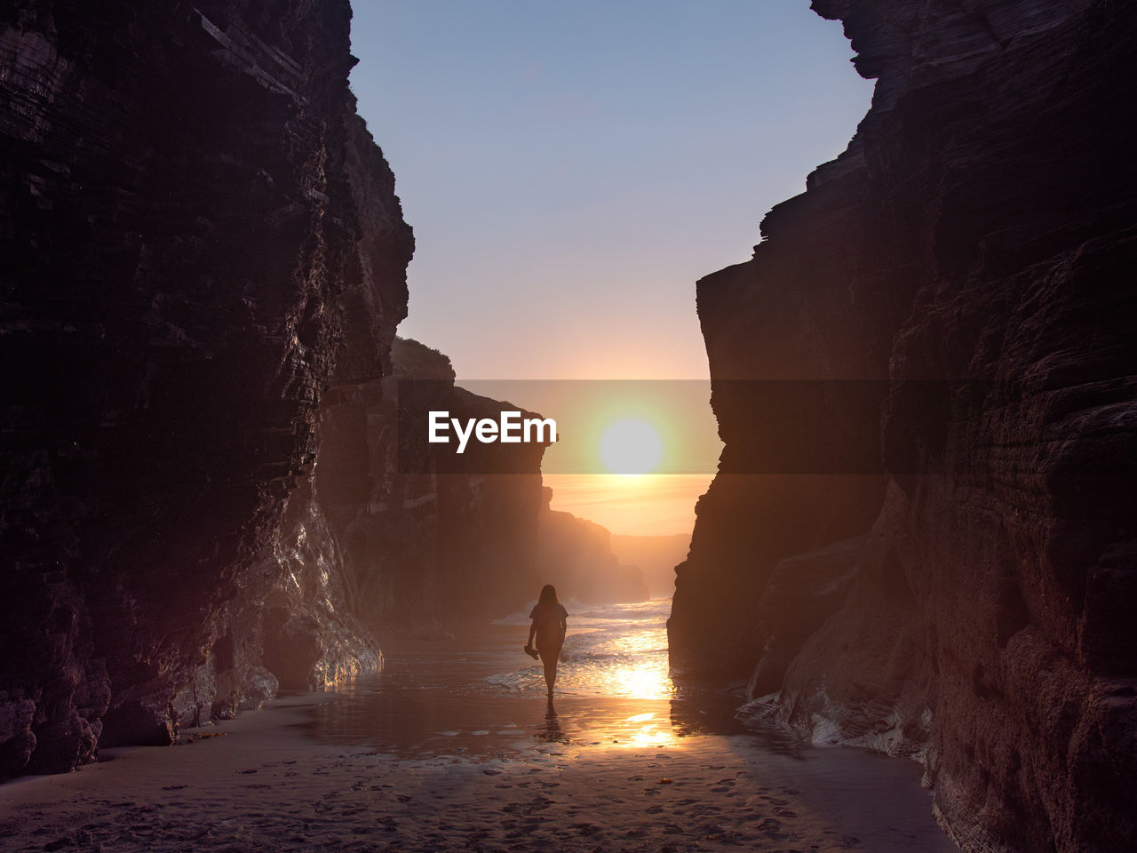 Rear view of woman standing at beach during sunset