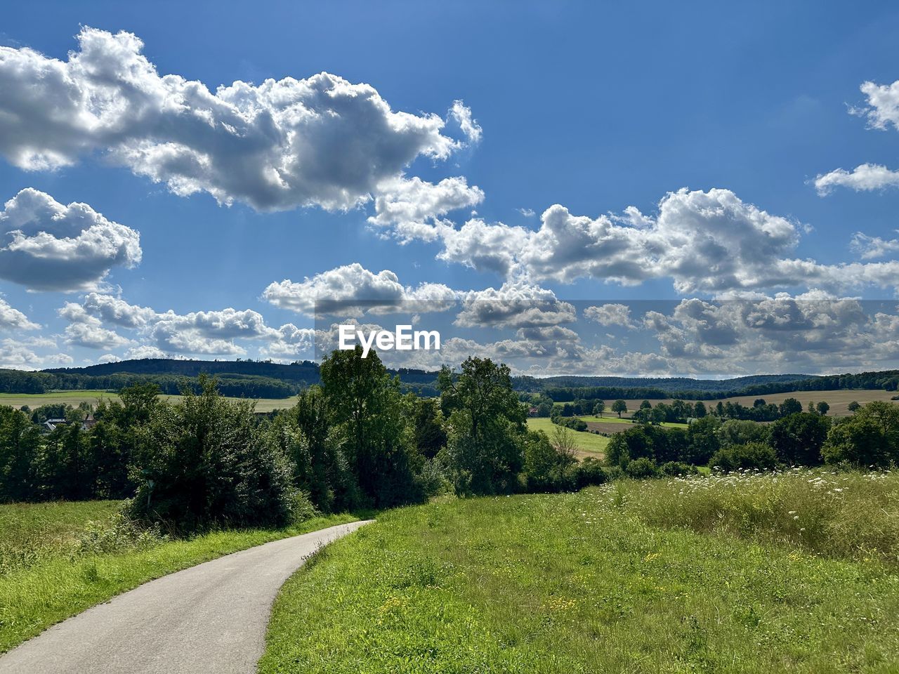 sky, landscape, plant, environment, cloud, nature, scenics - nature, grass, beauty in nature, tree, road, rural area, grassland, hill, land, meadow, horizon, no people, field, tranquility, green, plain, prairie, blue, tranquil scene, non-urban scene, rural scene, natural environment, travel, day, transportation, plateau, outdoors, travel destinations, mountain range, the way forward, pasture, sunlight, summer, forest, idyllic, growth, tourism, remote