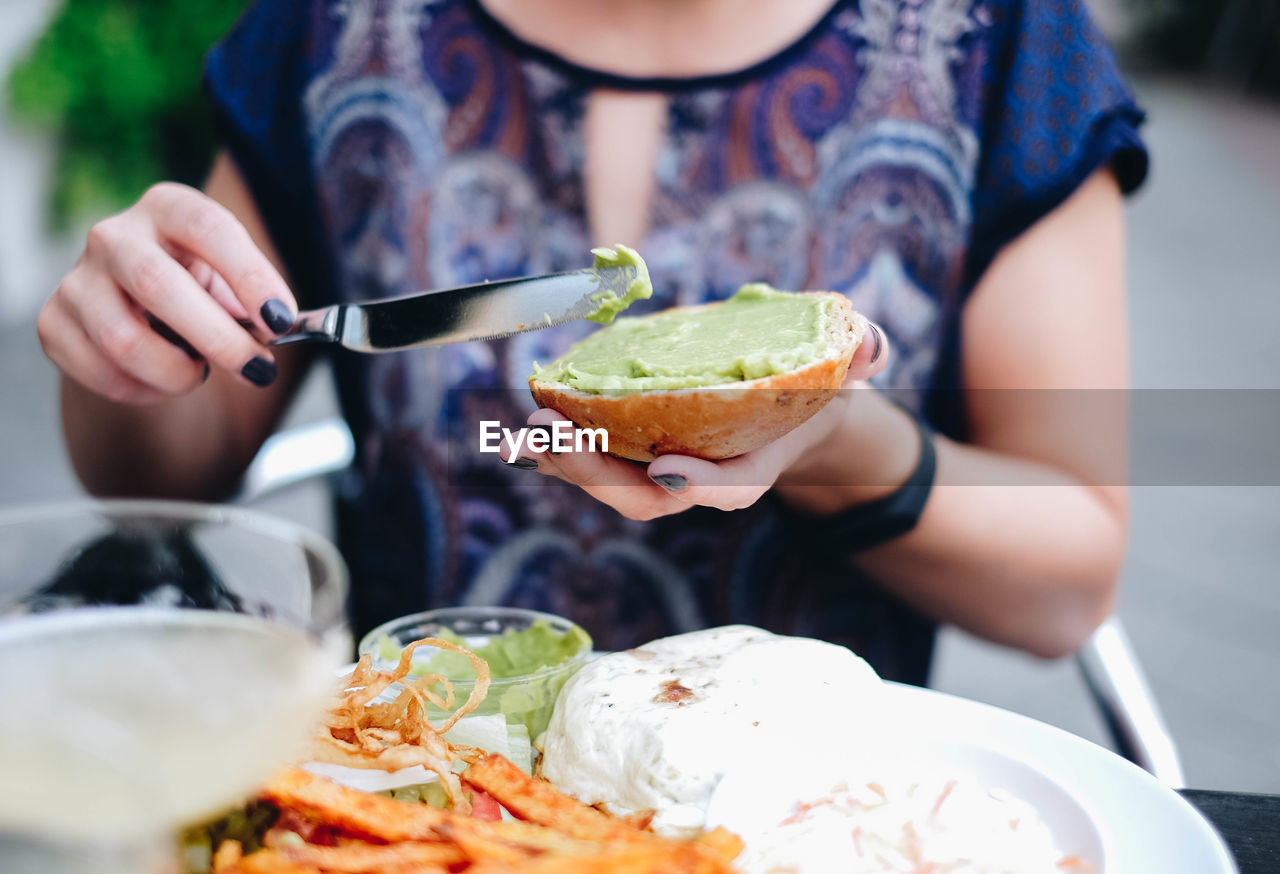 Midsection of woman applying sauce on bun in plate