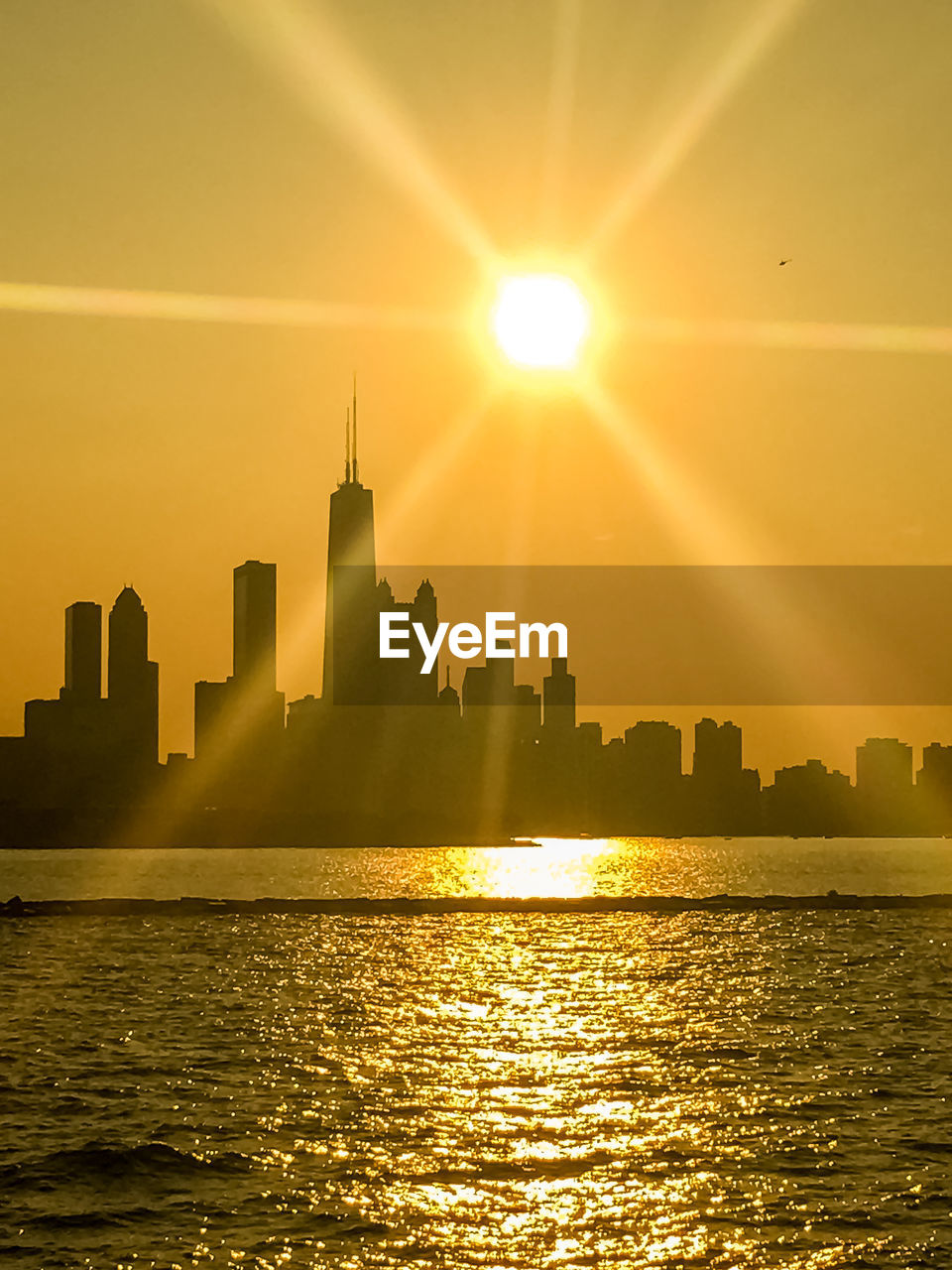 Sea by modern buildings against sky during sunset