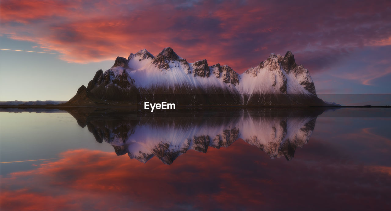 Scenic view of mountains by lake against dramatic sky during sunset