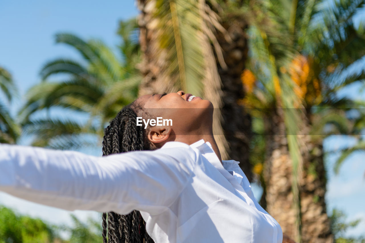 Happy african woman raising arms while facing the sun in a park