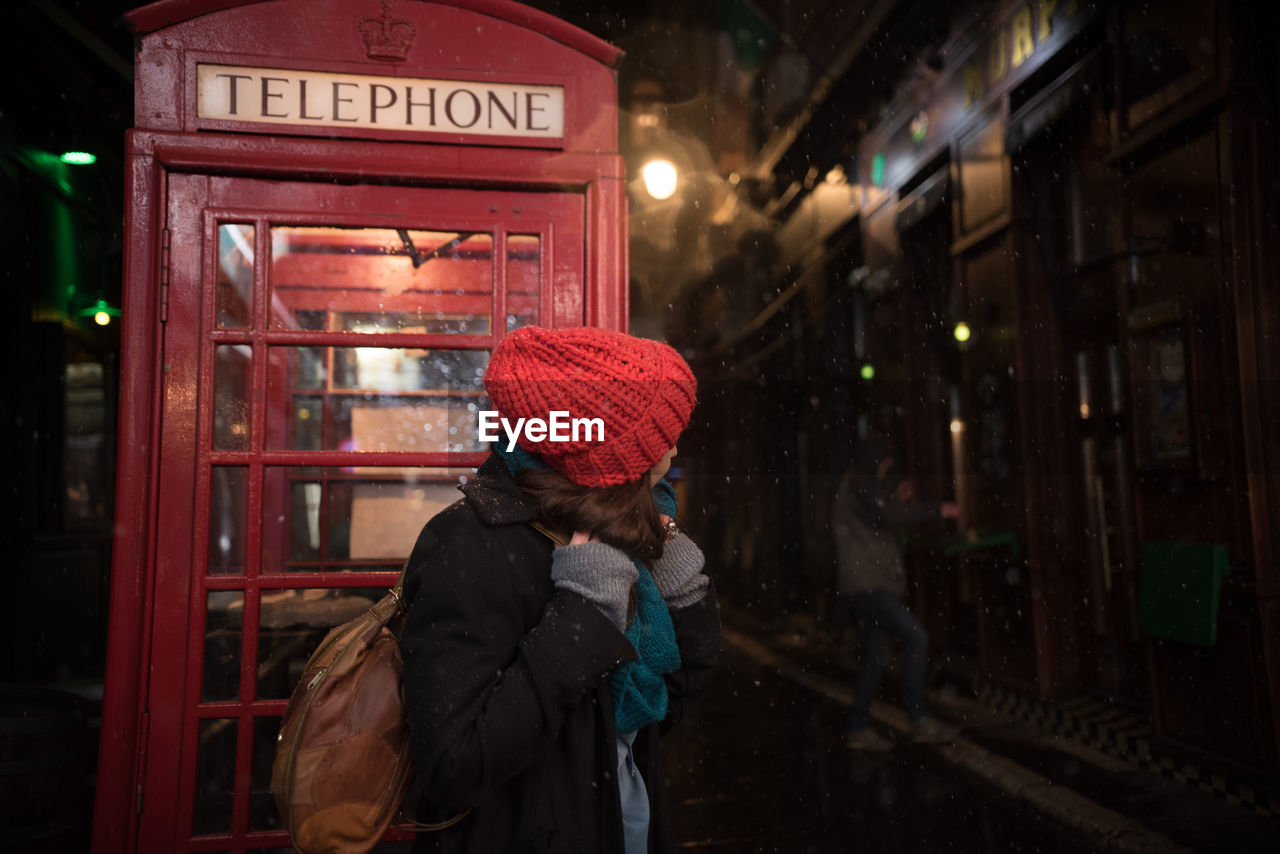 Woman standing against telephone booth at night