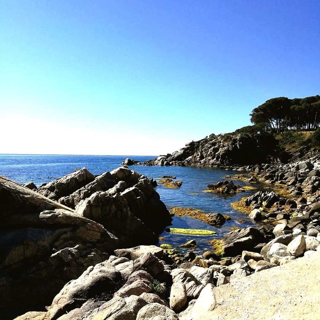 ROCKS BY SEA AGAINST CLEAR BLUE SKY