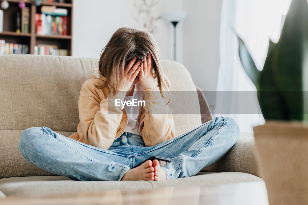 Tired schoolgirl girl sits on the couch and holds on with her hands. per head. children's stress 