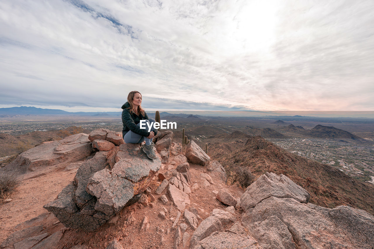 Full length of woman sitting on rock against sky