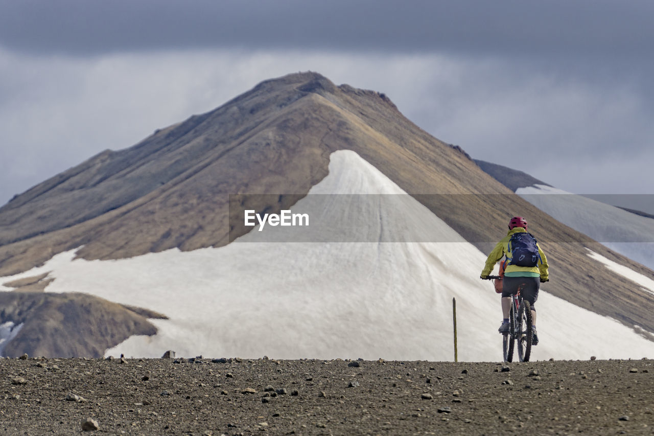 Rear view of person riding bicycle against snow covered mountain