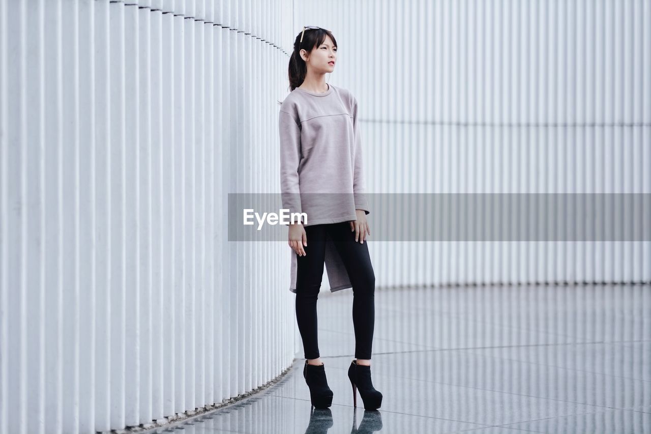 Full length of young woman standing by wall