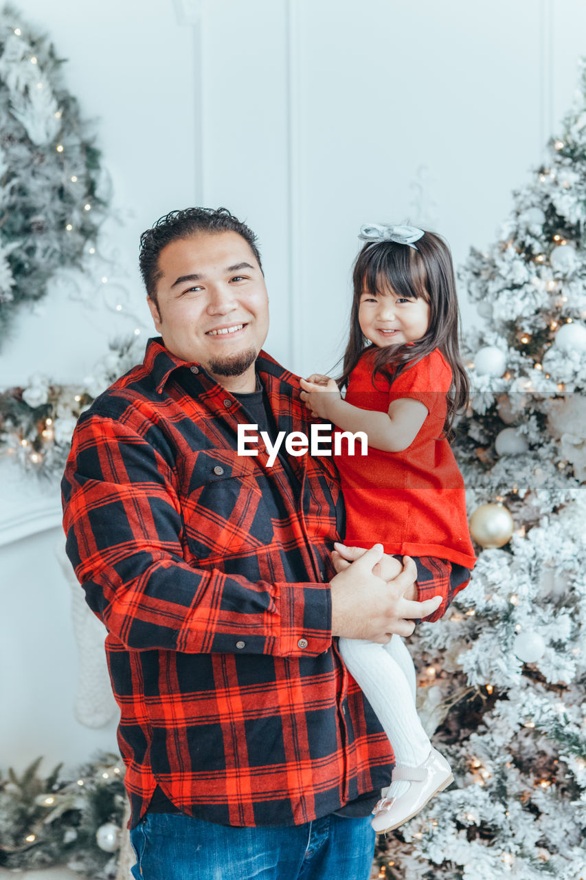 Portrait of smiling father and daughter against christmas tree